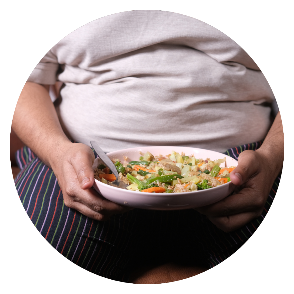Uma pessoa em estado de obesidade sentada ao sofa com um prato de comida na mão