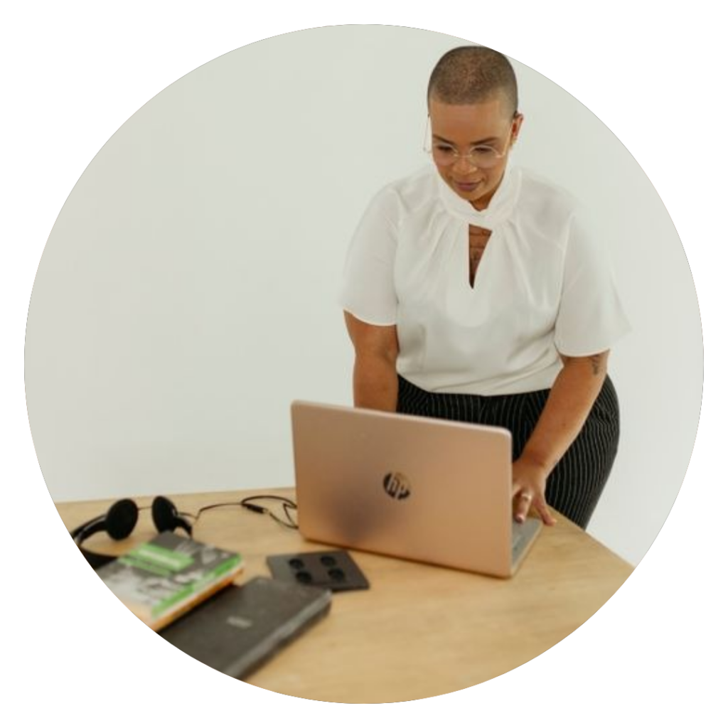 Psicologa Thais utilizando um notebook prateado em um fundo branco com uma camisa branca e uma calça preta